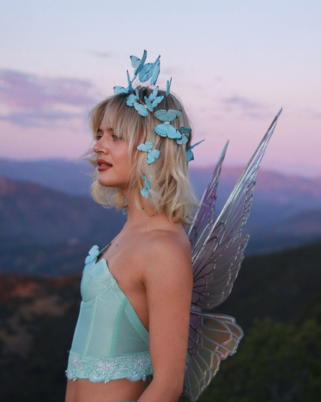 Person in fairy costume with butterfly headpiece and wings against a mountainous landscape