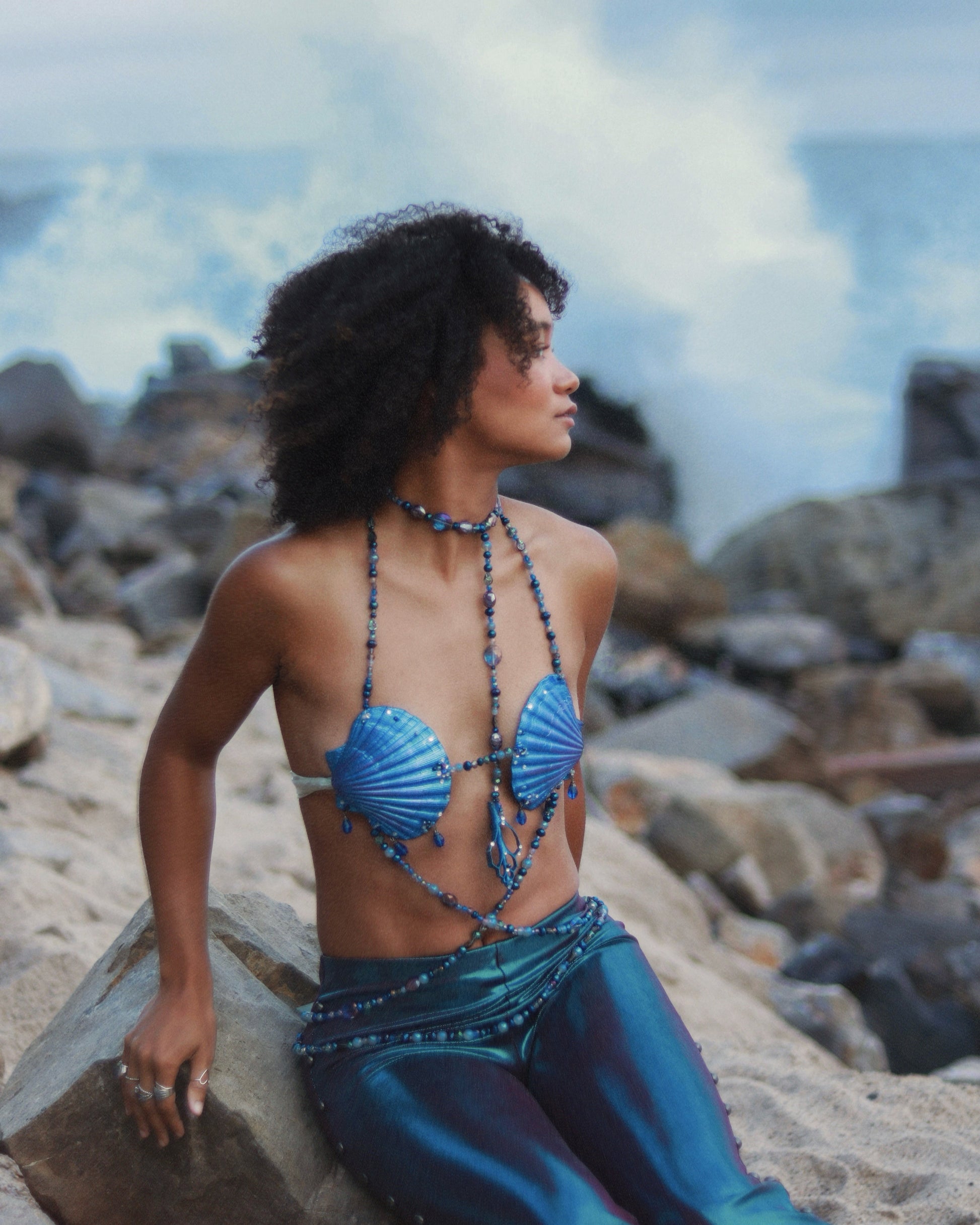 Person in a blue mermaid costume sitting on rocks with a scenic background
