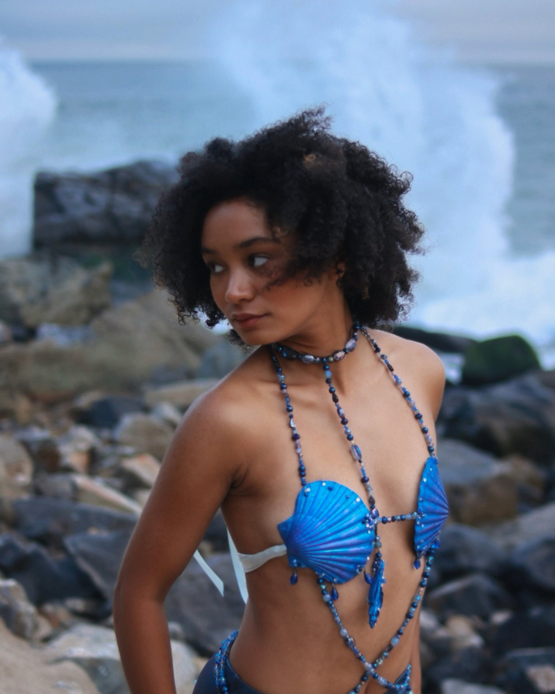 Woman wearing a blue bikini with seashell design against a rocky beach background