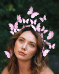 Woman wearing a headpiece with pink butterflies against a dark green leafy background